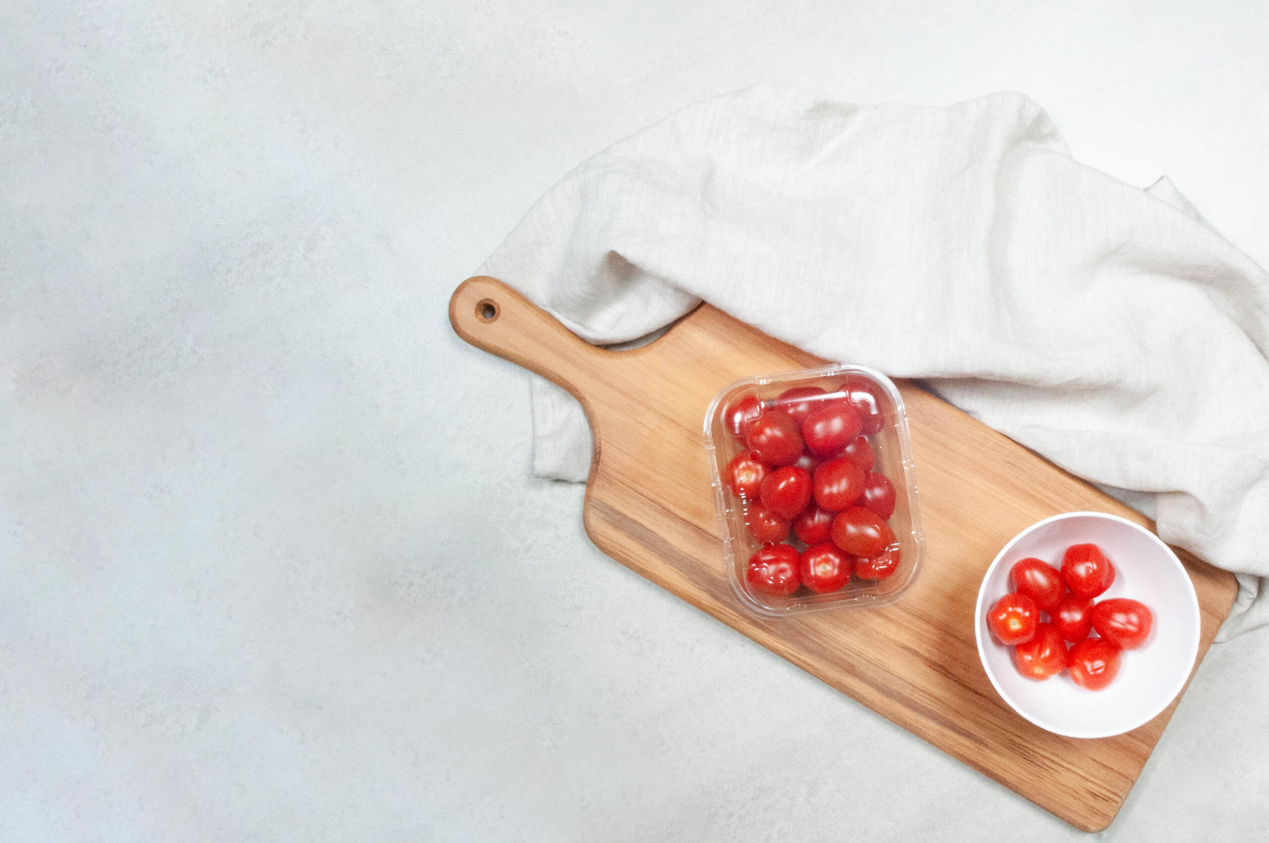 cherry tomatoes in plastic container on wooden chopping board