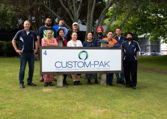 group of people standing outside together holding a large banner with custompak logo